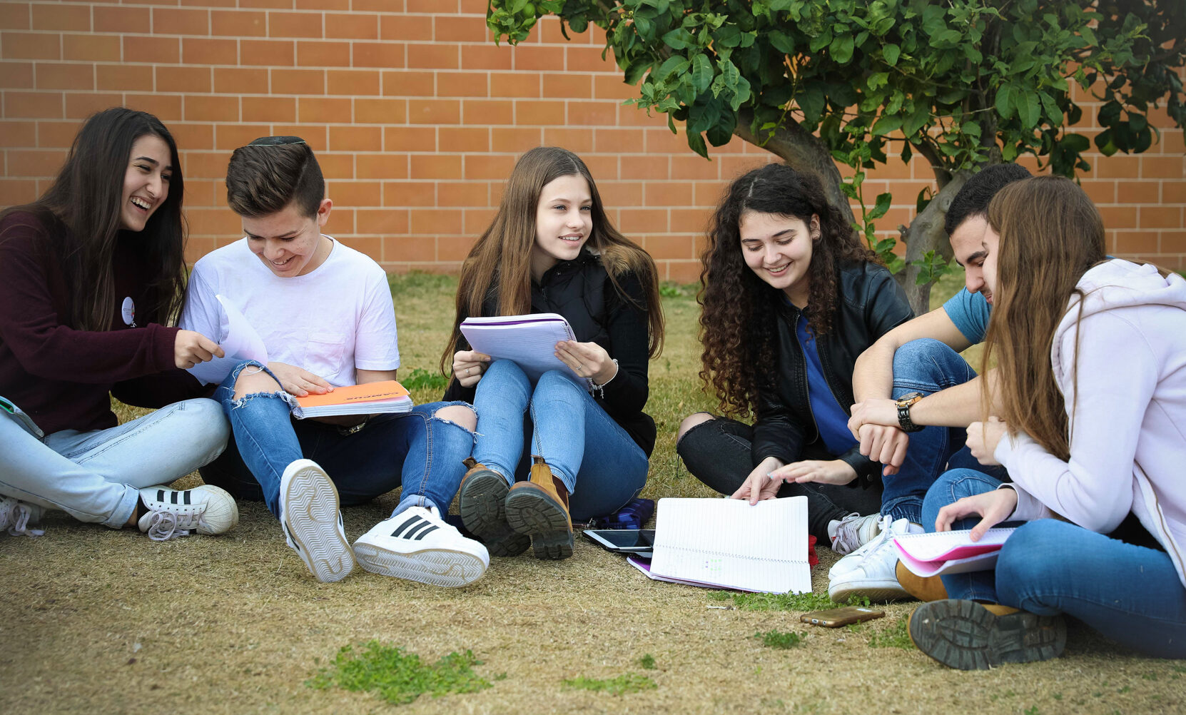 Israeli high school students study and talk on a patch of grass outside their school.