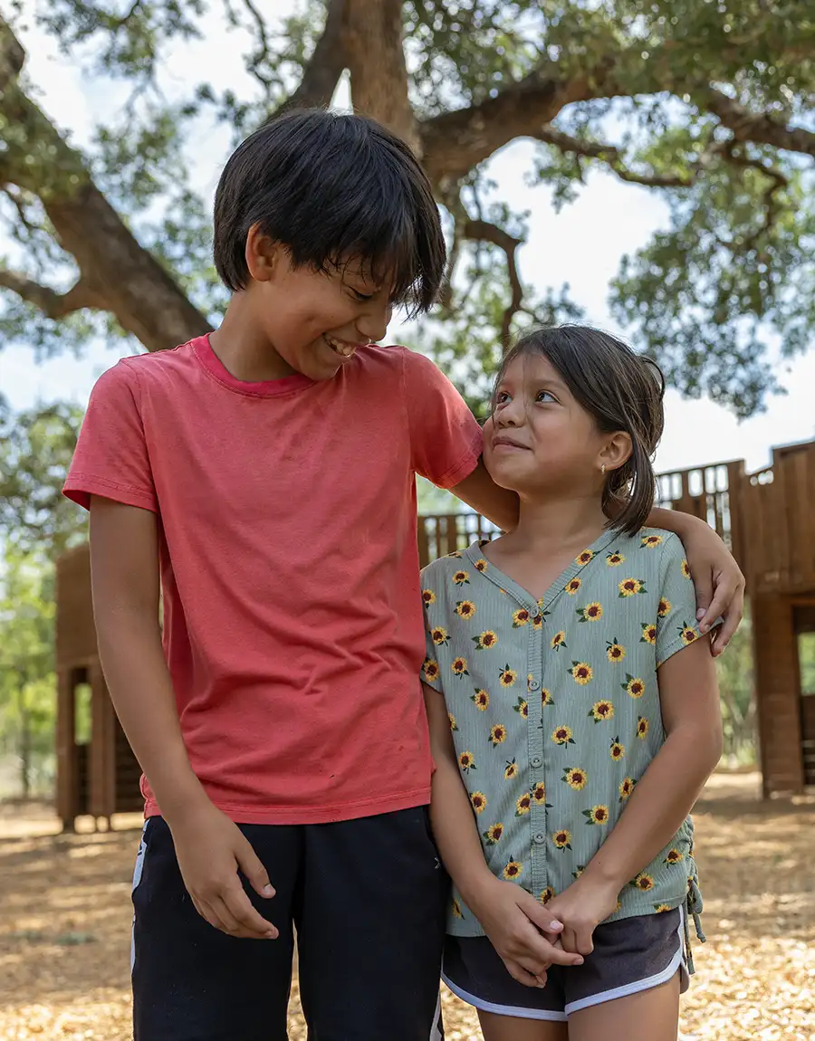Two children smiling looking at each other, standing inside a playground